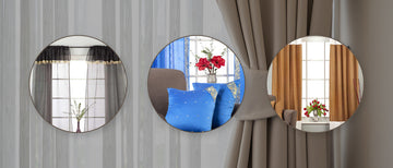 Three circular wall mirrors mounted on a gray curtain panel, reflecting different interior room scenes with windows, drapes, blue pillows, and red flowers.